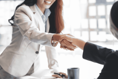 A business woman standing and shaking hands with another business woman who is sitting down