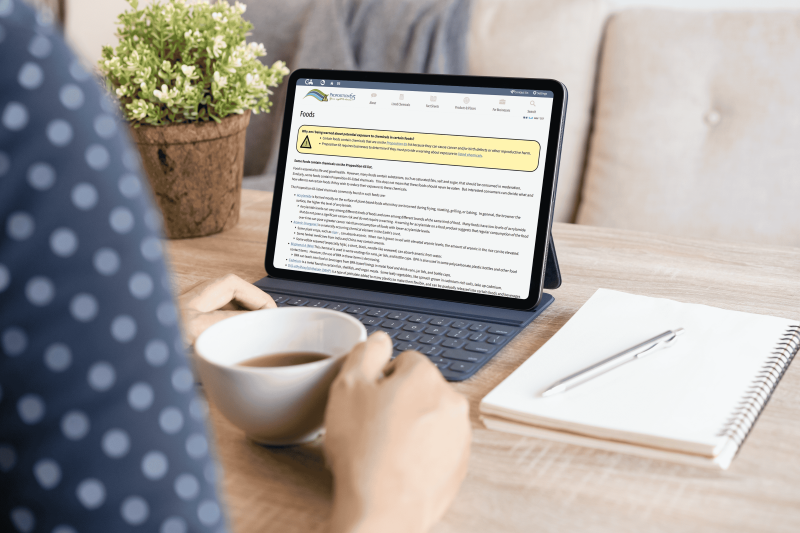 A woman drinking coffee looking at a computer screen which shows a Proposition 65 fact sheet.