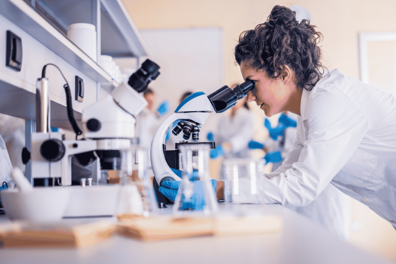 A woman in a lab coat looking into a microscope in a laboratory.