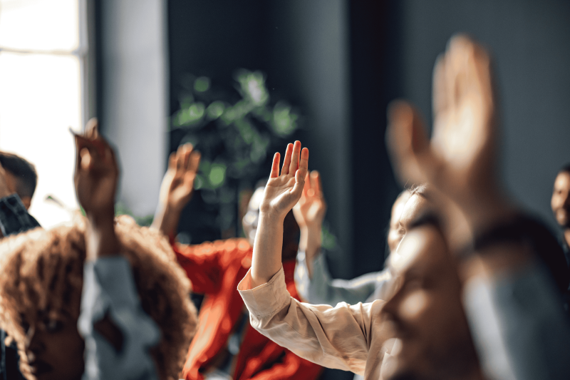 People in a room sitting down and raising their hands to ask a question.